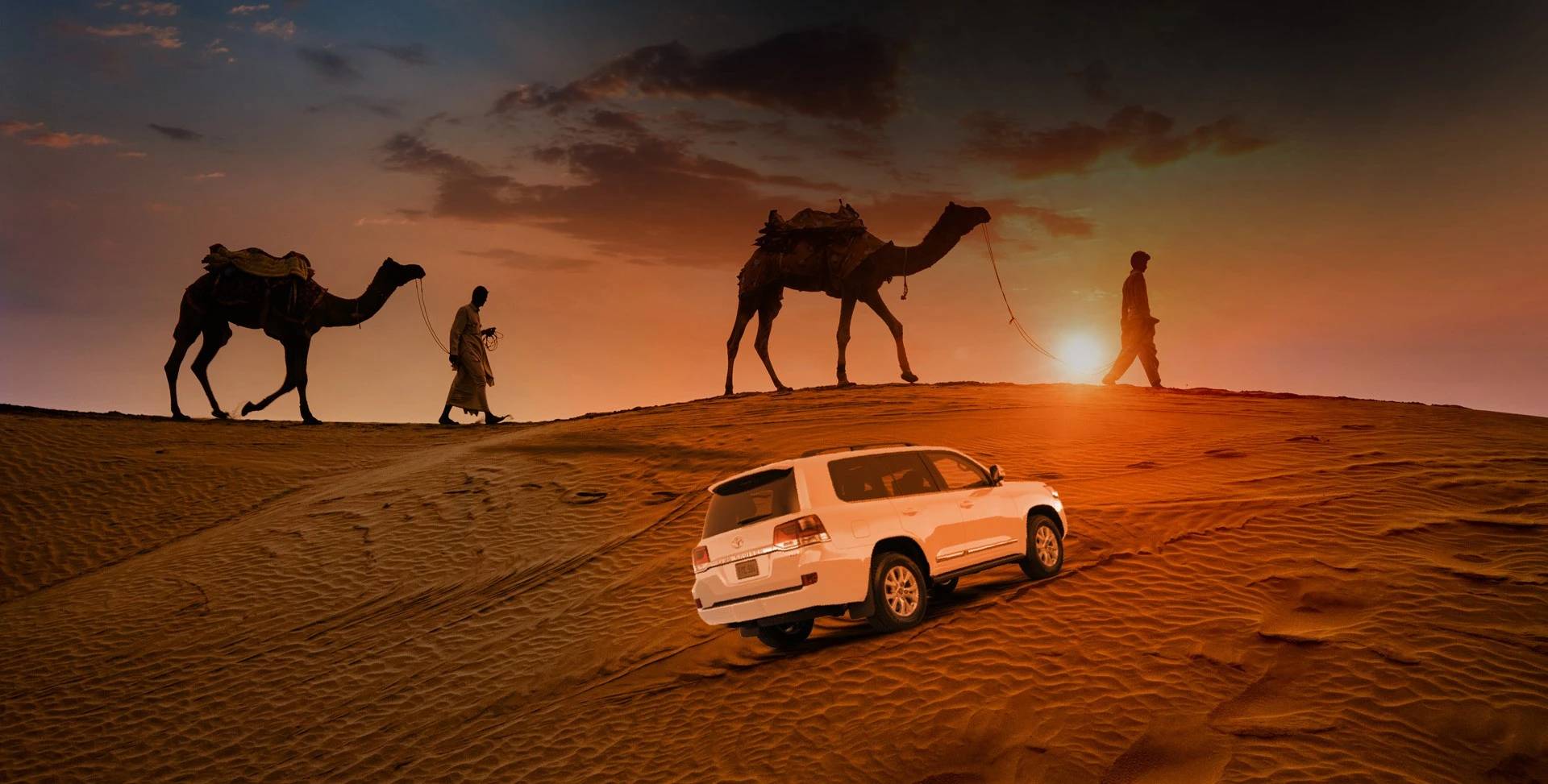 Sunset over Al Khatim Desert Safari, camels and SUV on sand dunes.