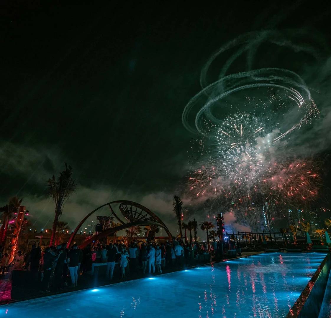Fireworks over Be Beach DXB, Dubai, with poolside crowd.