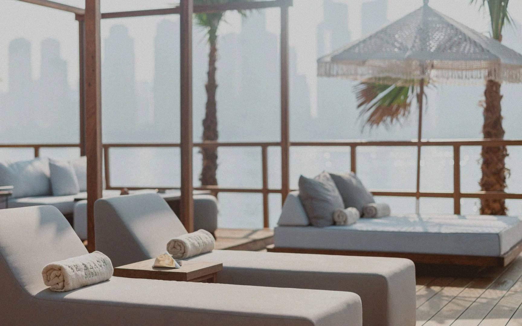Lounge chairs at Be Beach DXB, Dubai, with city skyline view.