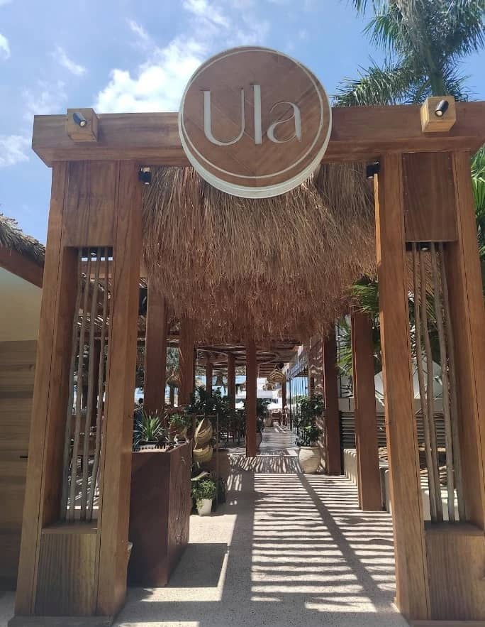 Entrance of Ula Dubai Beach Club with wooden decor and plants.