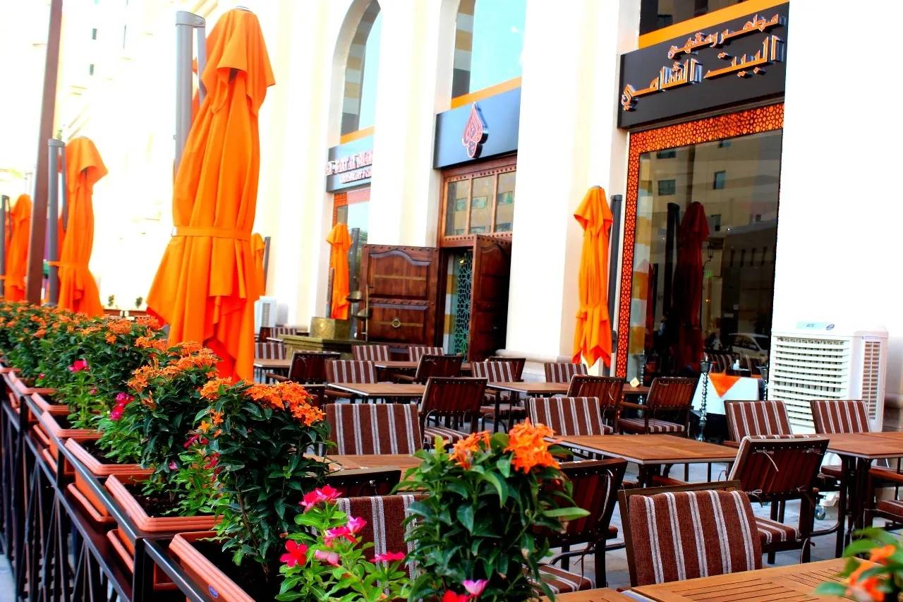 Outdoor seating at Al Bait Al Shami Restaurant, Dubai with orange umbrellas.