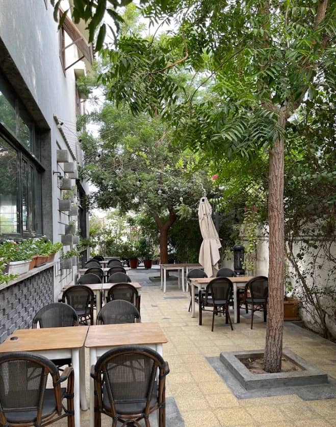 Outdoor seating area at Mamaesh Al Manara, Dubai, with trees and tables.