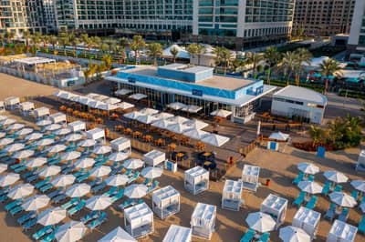 Beachfront view of Hilton Dubai Palm Jumeirah with umbrellas and loungers.