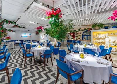 Opa Dubai dining room with blue chairs and vibrant floral arrangements.