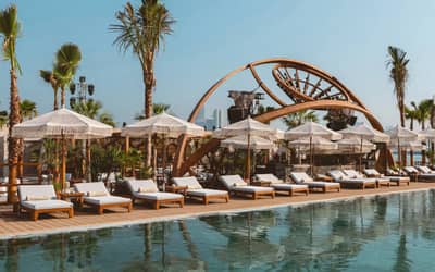 Be Beach DXB Dubai poolside loungers with umbrellas and palm trees.
