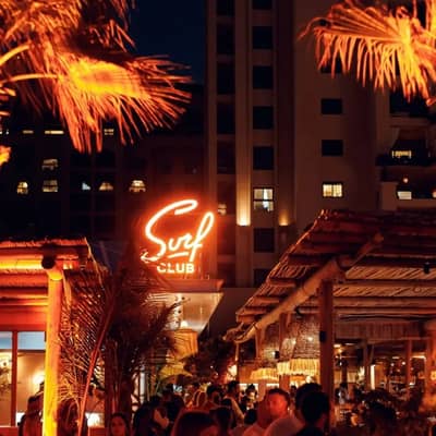 Surf Club Dubai at night with neon lights and palm trees.