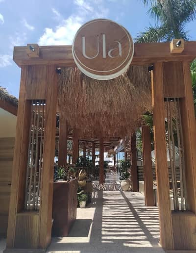 Entrance of Ula Dubai Beach Club with wooden decor and plants.
