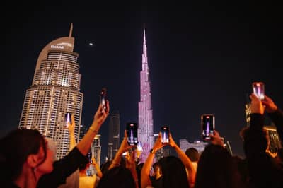 Crowd photographing illuminated skyscrapers at night in Dubai, UAE.