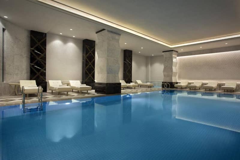 Lazzoni Hotel - a hotel lobby with a large swimming pool with white chairs at Lazzoni Hotel in Istanbul