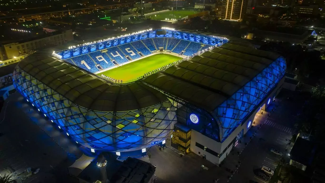Aerial view of Al Nasr Al Maktoum Stadium, Dubai, illuminated at night.